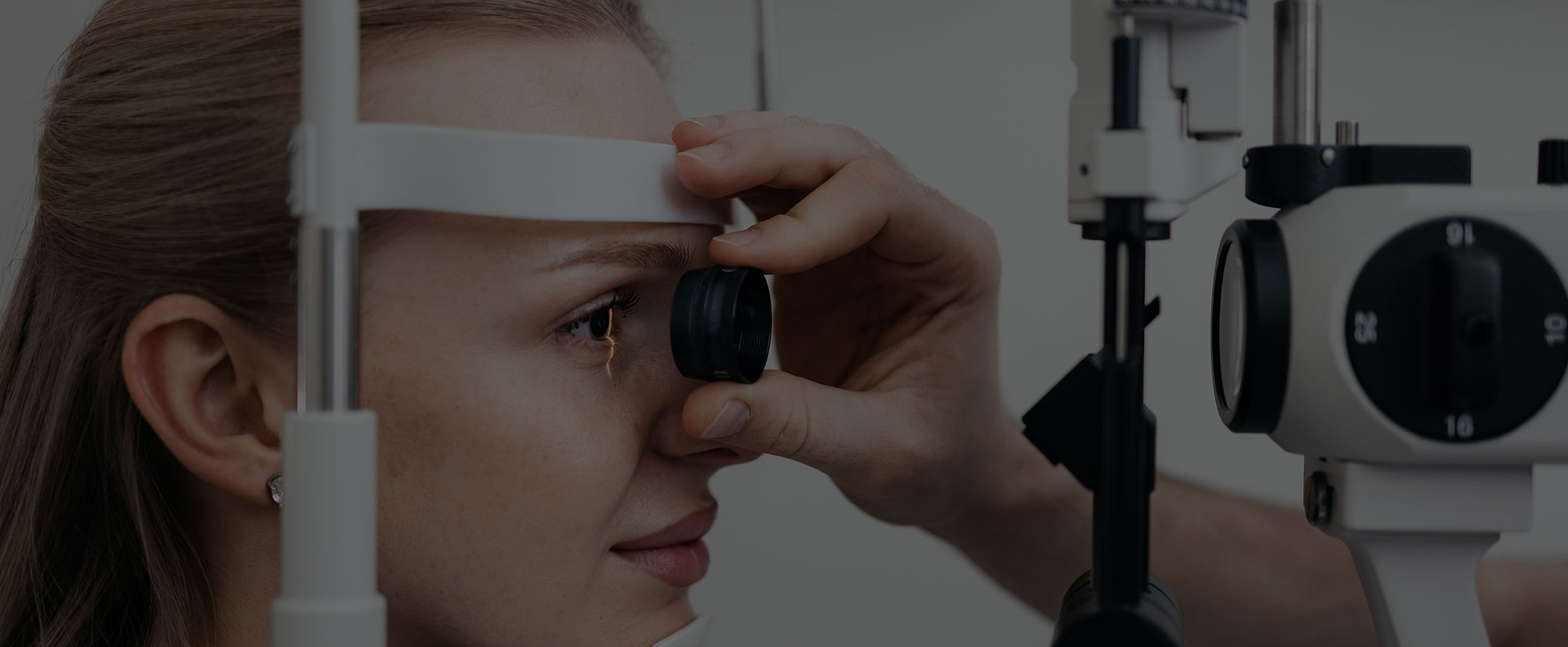 Eye doctor examining a woman's retina at a slit lamp with a handheld lens