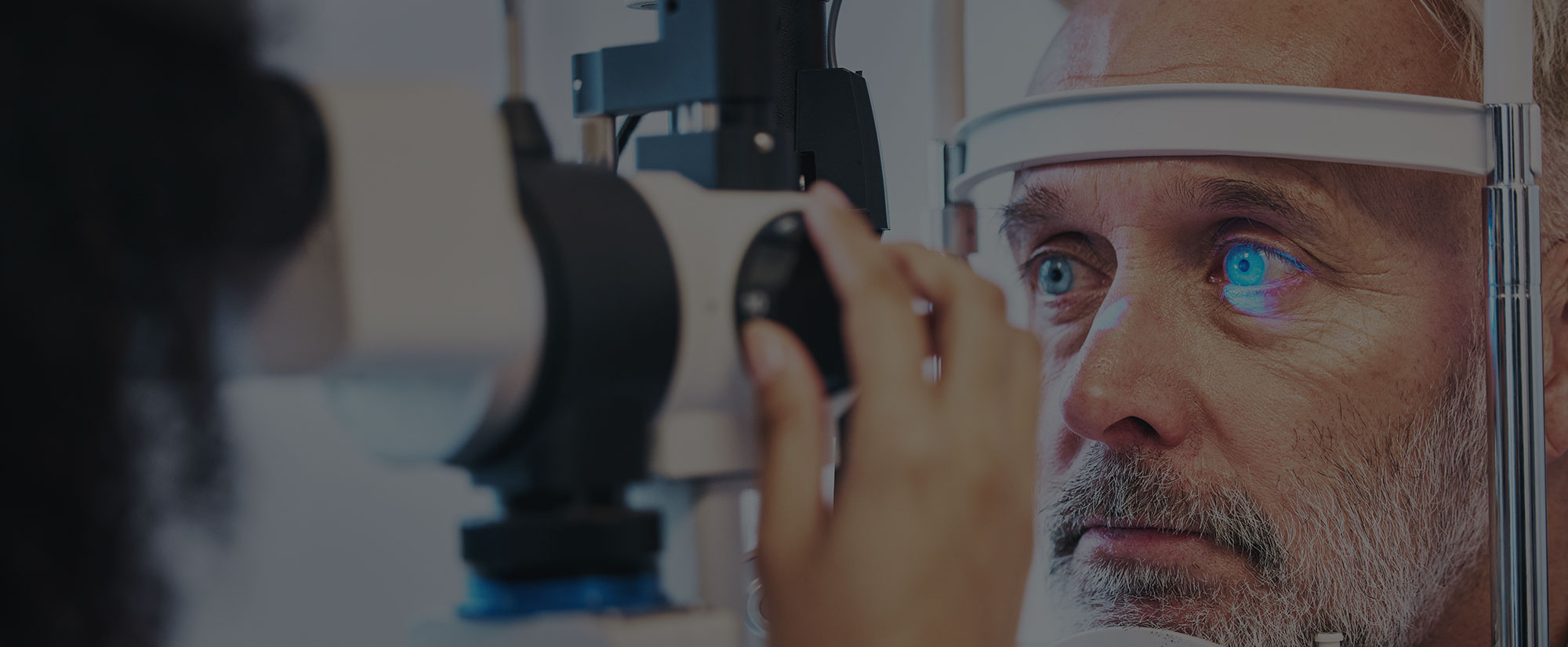 Eye doctor examining an older man's eye at a slit lamp during a glaucoma check